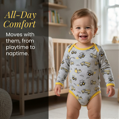 A smiling baby boy wearing a gray and yellow onesie with a truck pattern, standing in a nursery setting.
