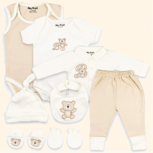 A collection of baby clothing and accessories, including a onesie, a shirt, pants, a hat, a bib, and mittens, all featuring a teddy bear design.