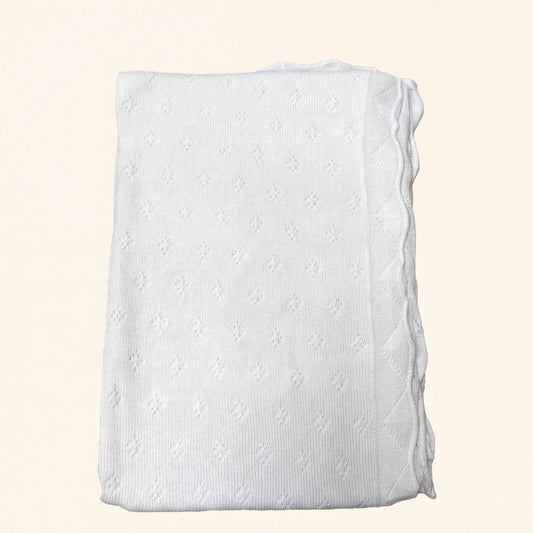 A white knitted blanket with a scalloped edge is shown against a light background.