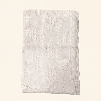 A cream-colored knitted blanket with a geometric pattern.