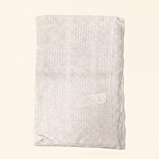 A cream-colored knitted blanket with a geometric pattern.