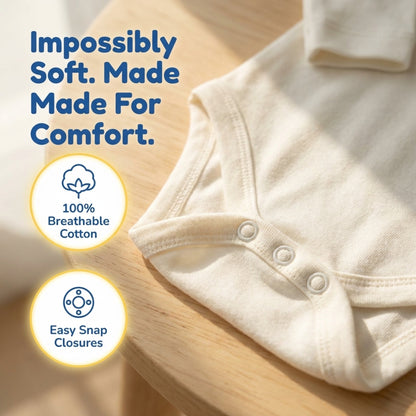 The image is a close-up of a white baby onesie, highlighting its soft and comfortable material. The text above the onesie reads "Impossibly Soft. Made For Comfort." The onesie is shown on a wooden surface, and there are two icons indicating 100% breathable cotton and easy snap closures.
