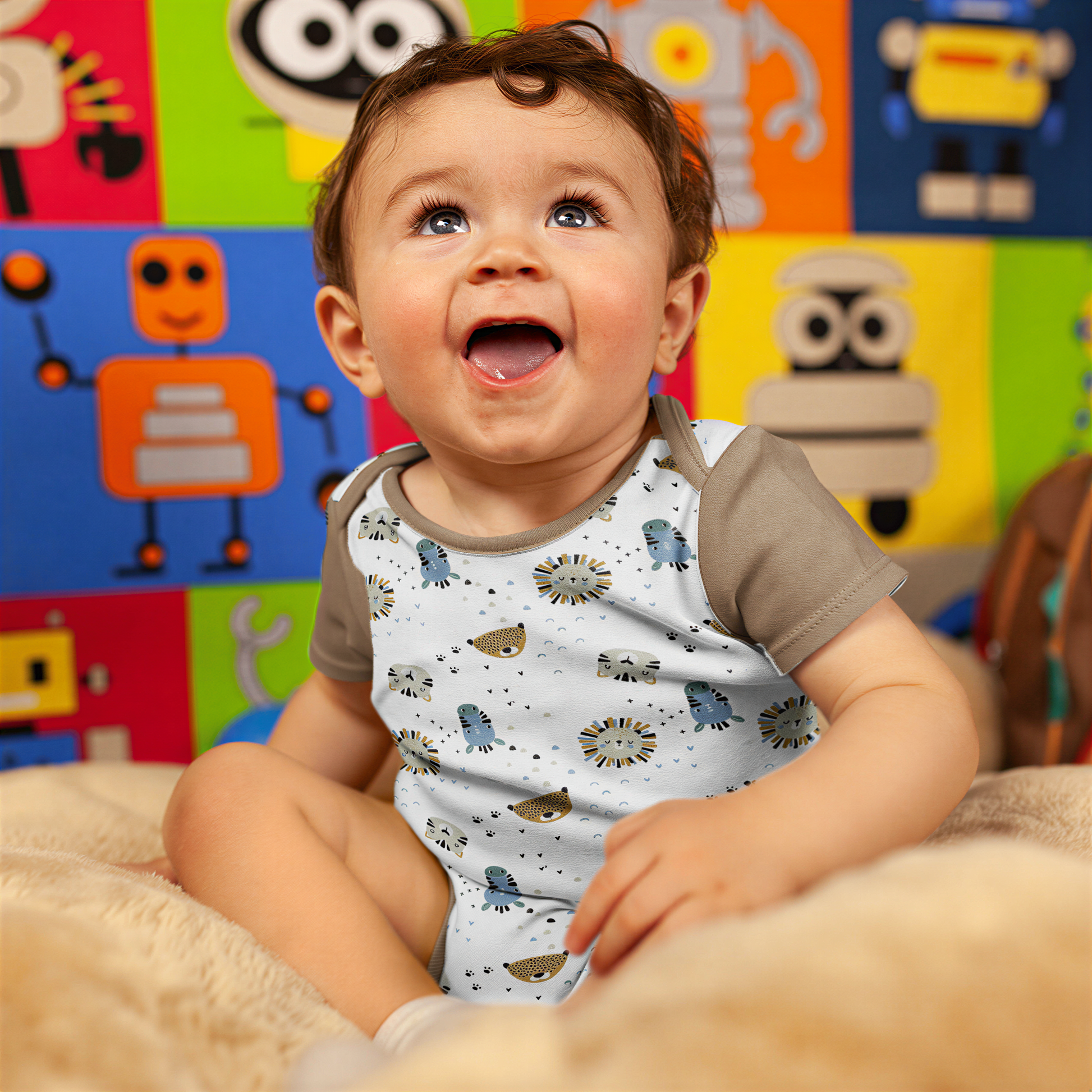 A smiling baby boy sitting on a bed, wearing a white onesie with animal designs.