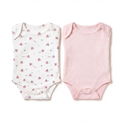 two baby onesies, one white with a pattern of hearts and one pink with polka dots, both laid out on a white background.